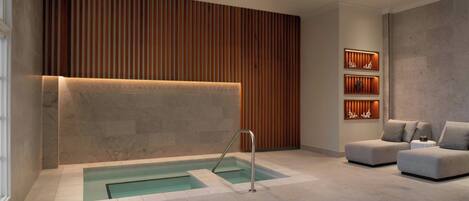 A modern spa area with a heated floor, a small pool, and a seating area with a wooden slat wall and shelves.