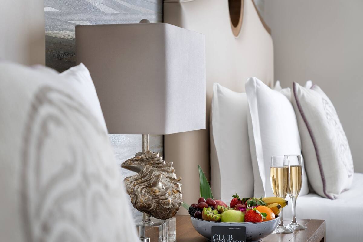 A well-appointed room with a modern lamp, a decorative shell, a fruit bowl, and two glasses of champagne on a wooden table.