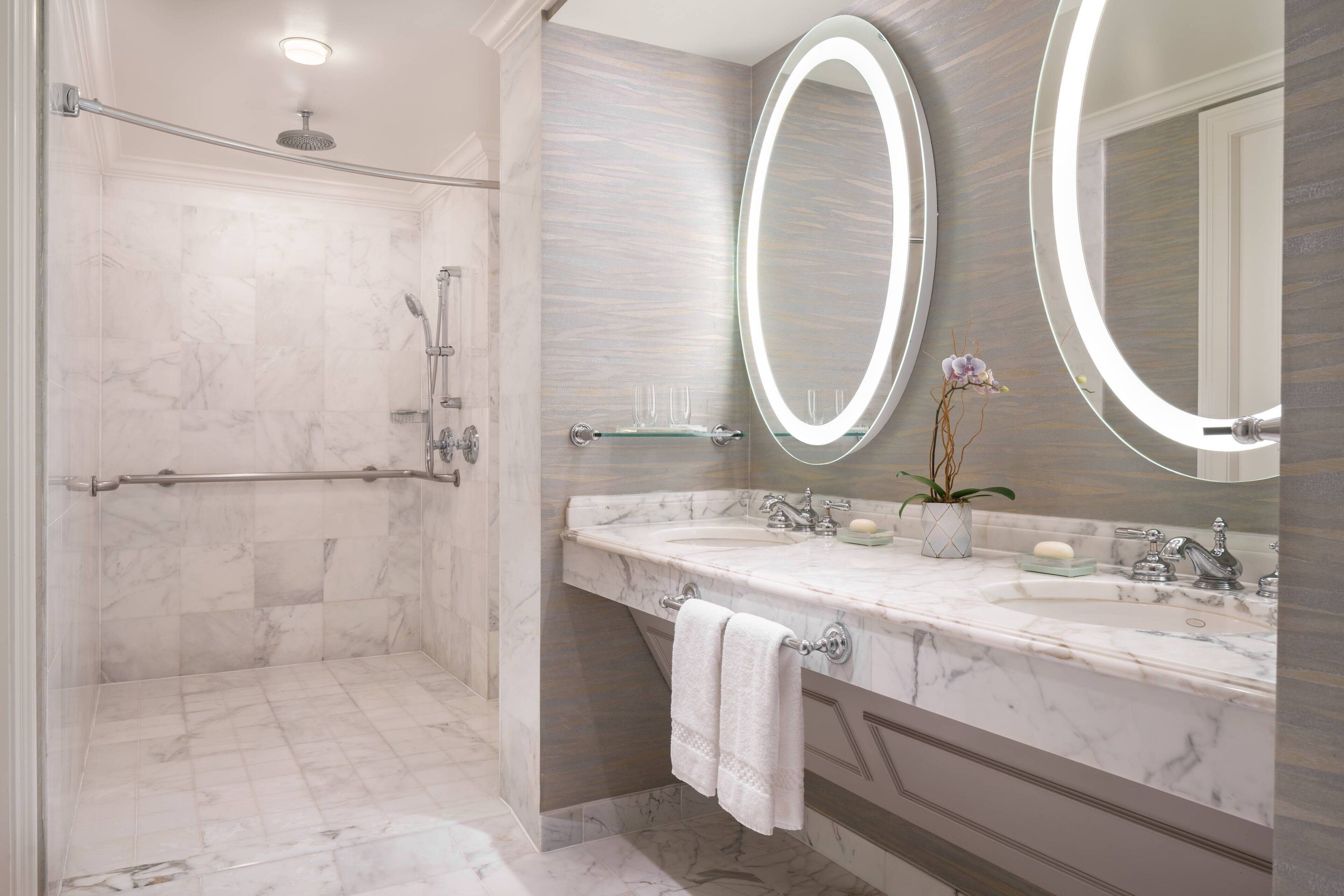 A modern bathroom with a walk-in shower, two large mirrors, a marble sink, and a glass shower enclosure.