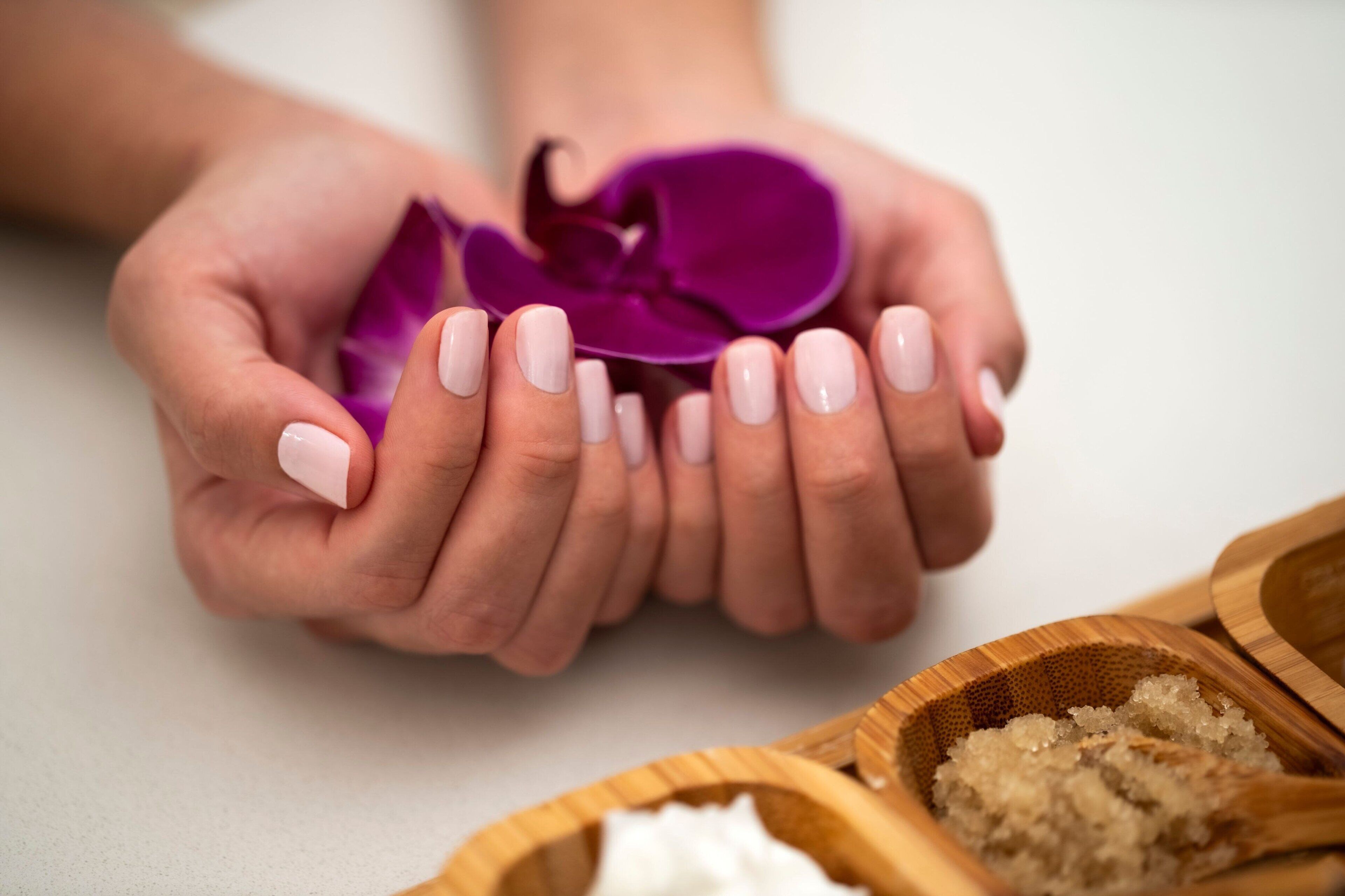 Des mains tenant une fleur violette, avec un bol en bois contenant des substances blanches et brunes.