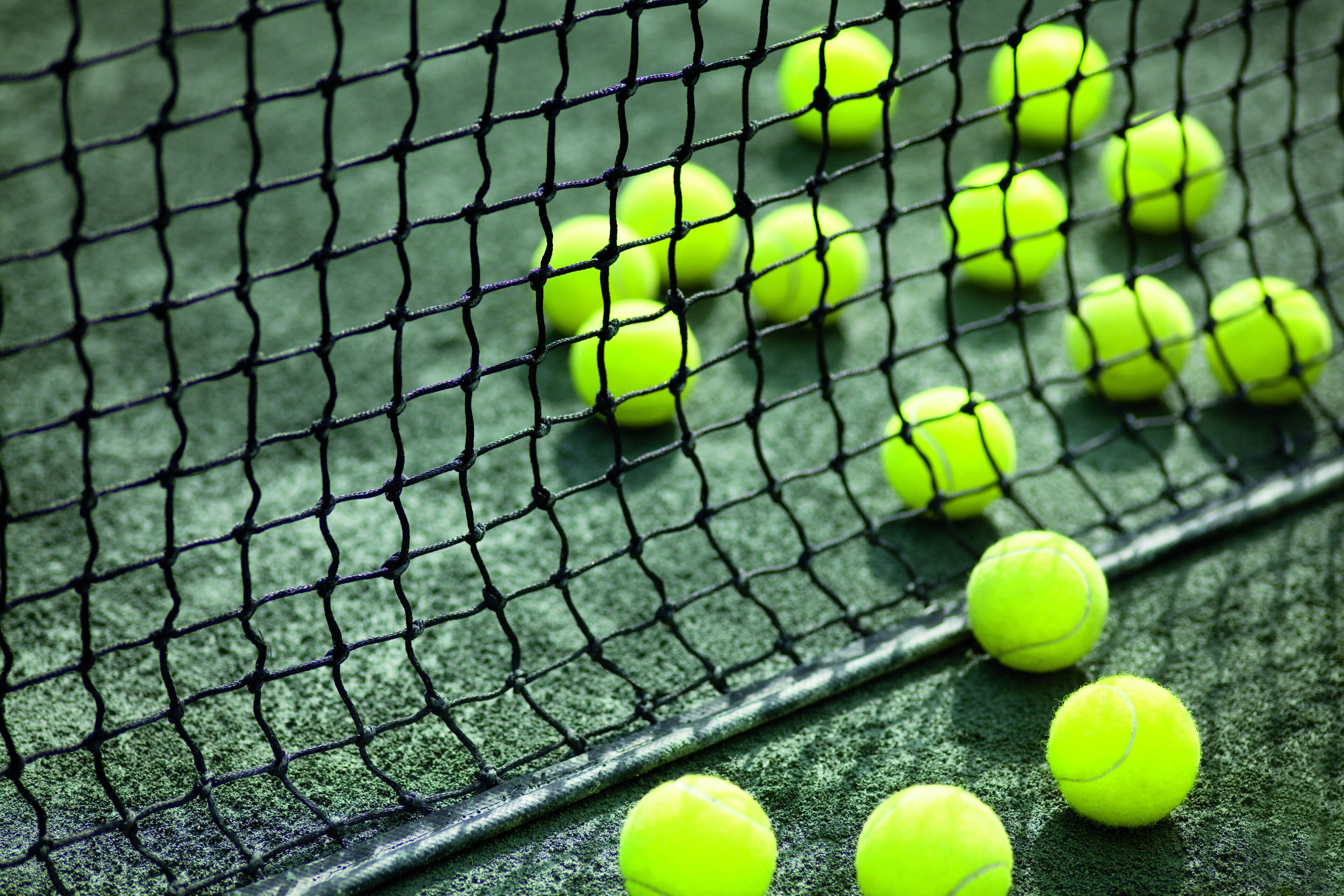 A tennis court with a net and multiple tennis balls.