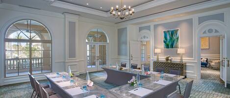 A spacious conference room with a large island table, multiple chairs, and a chandelier.