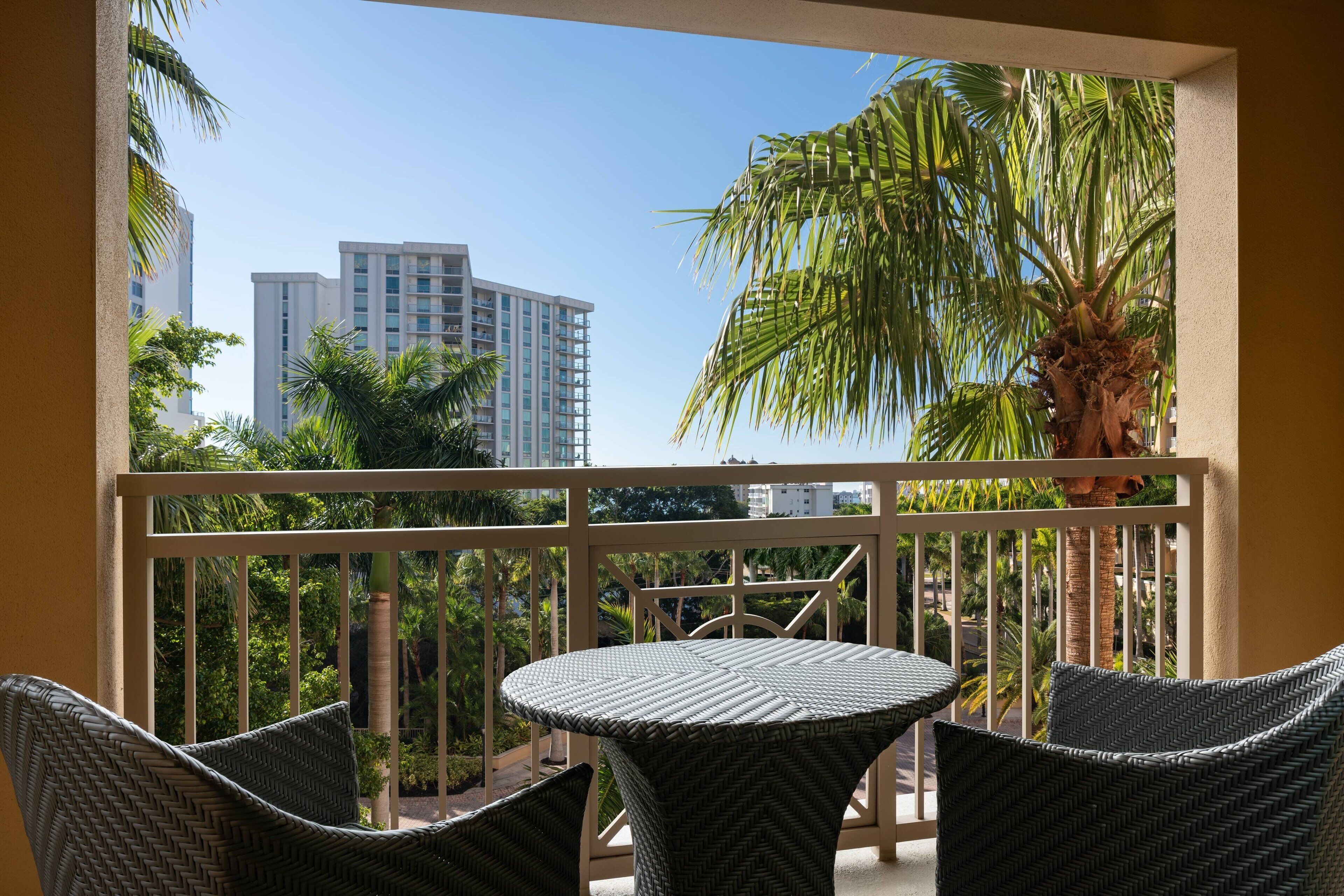 A balcony with wicker furniture, a view of palm trees, and tall buildings in the background.