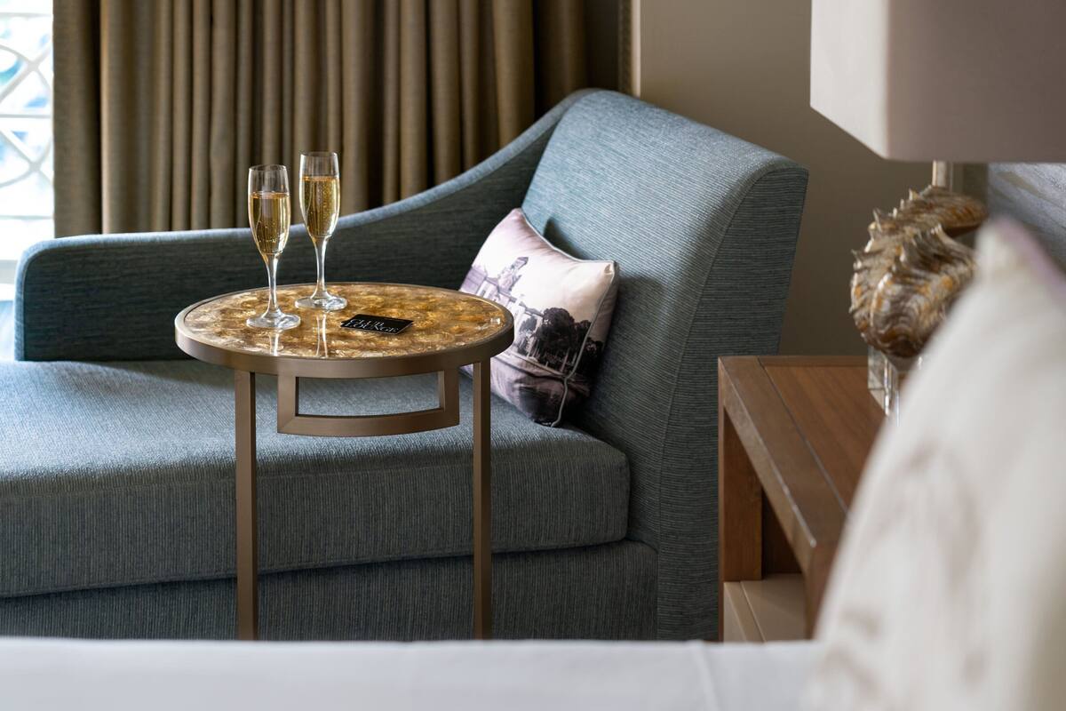 A modern room with a grey sofa, a round wooden table with two glasses of champagne, and a decorative pillow.