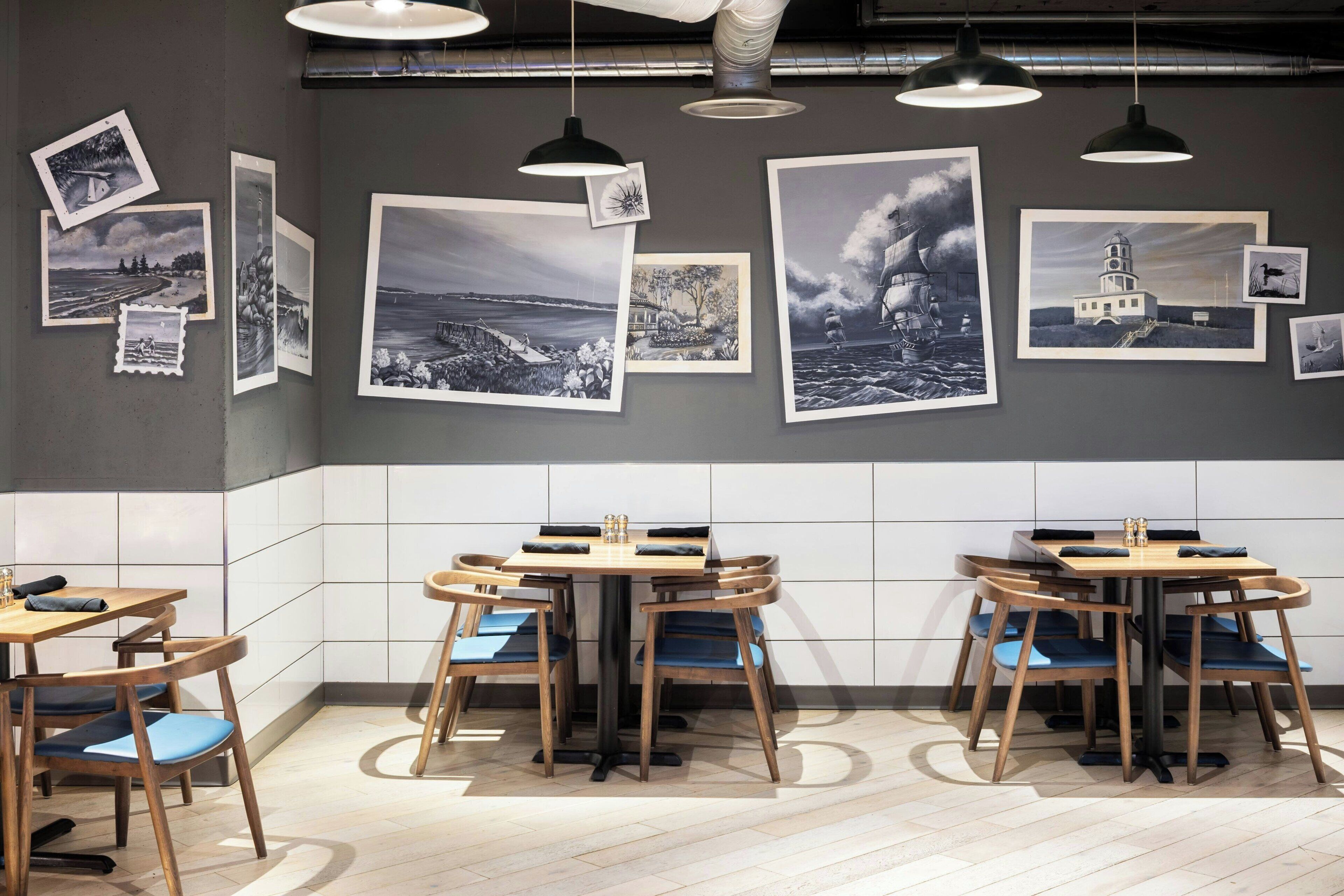 A modern dining area with wooden tables and chairs, a tiled backsplash, and black-and-white photographs on the wall.
