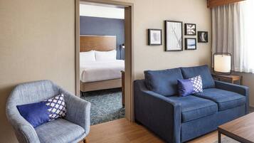 A hotel room with a bed, a blue sofa, a grey armchair, and a wooden coffee table.