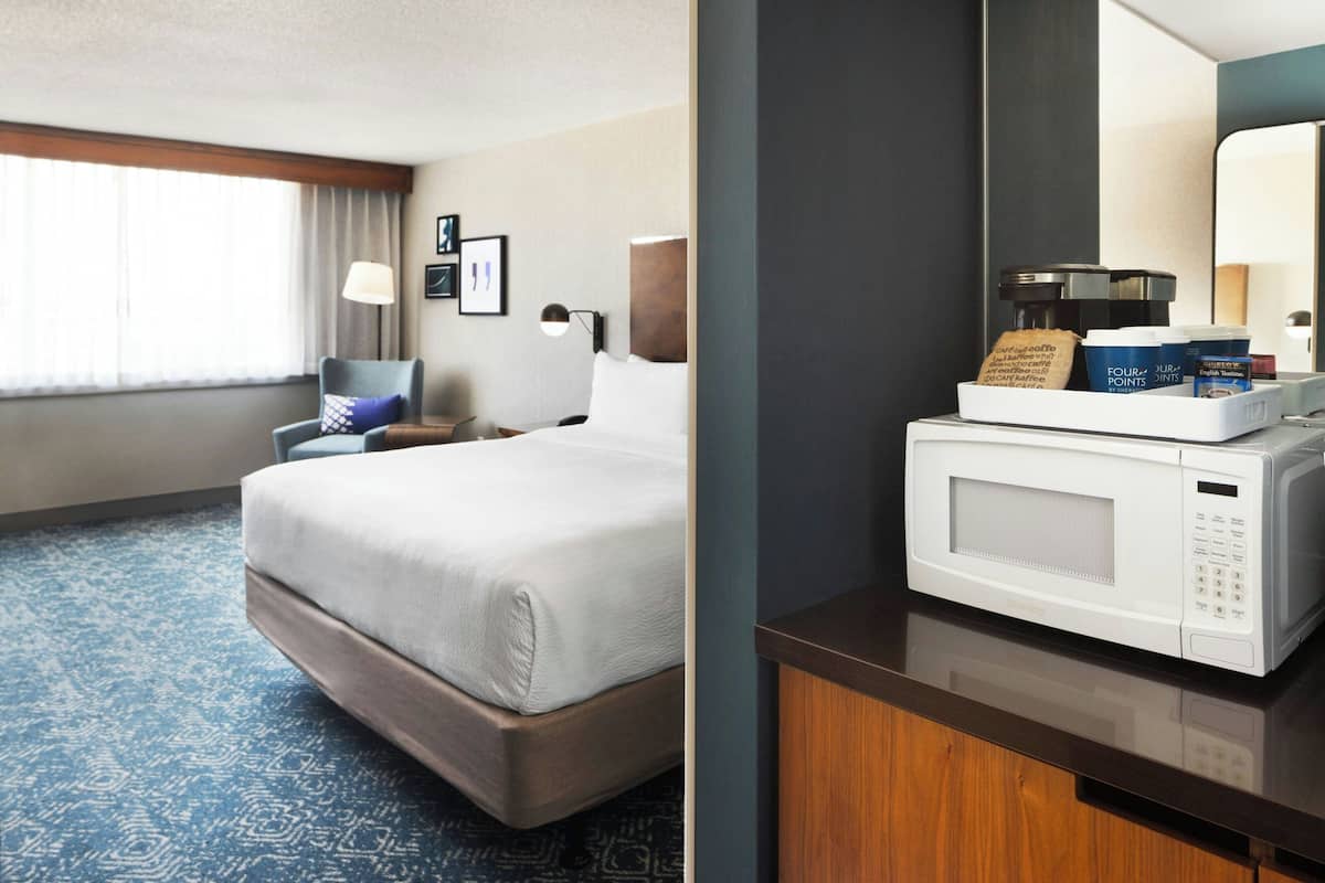 A hotel room with a bed, a nightstand, a lamp, a microwave, and a coffee maker.