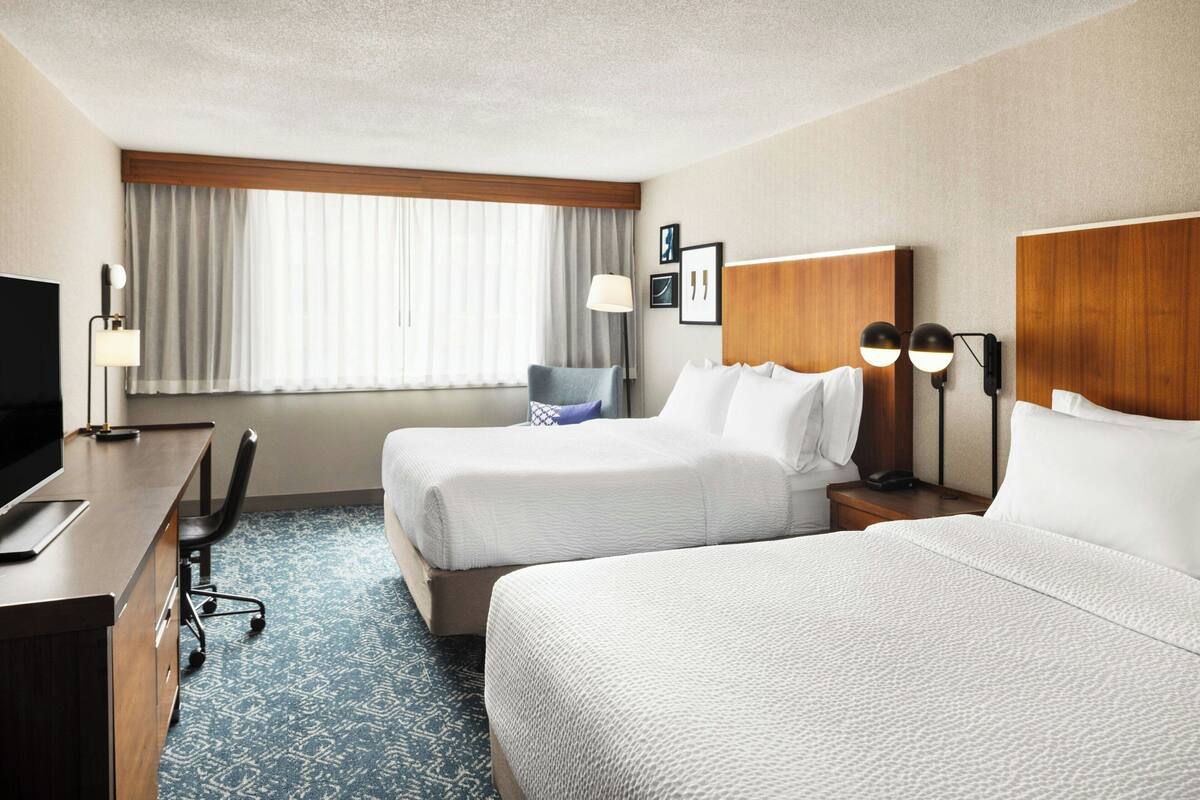 A hotel room with two beds, a desk, a chair, a TV, and a window with curtains.