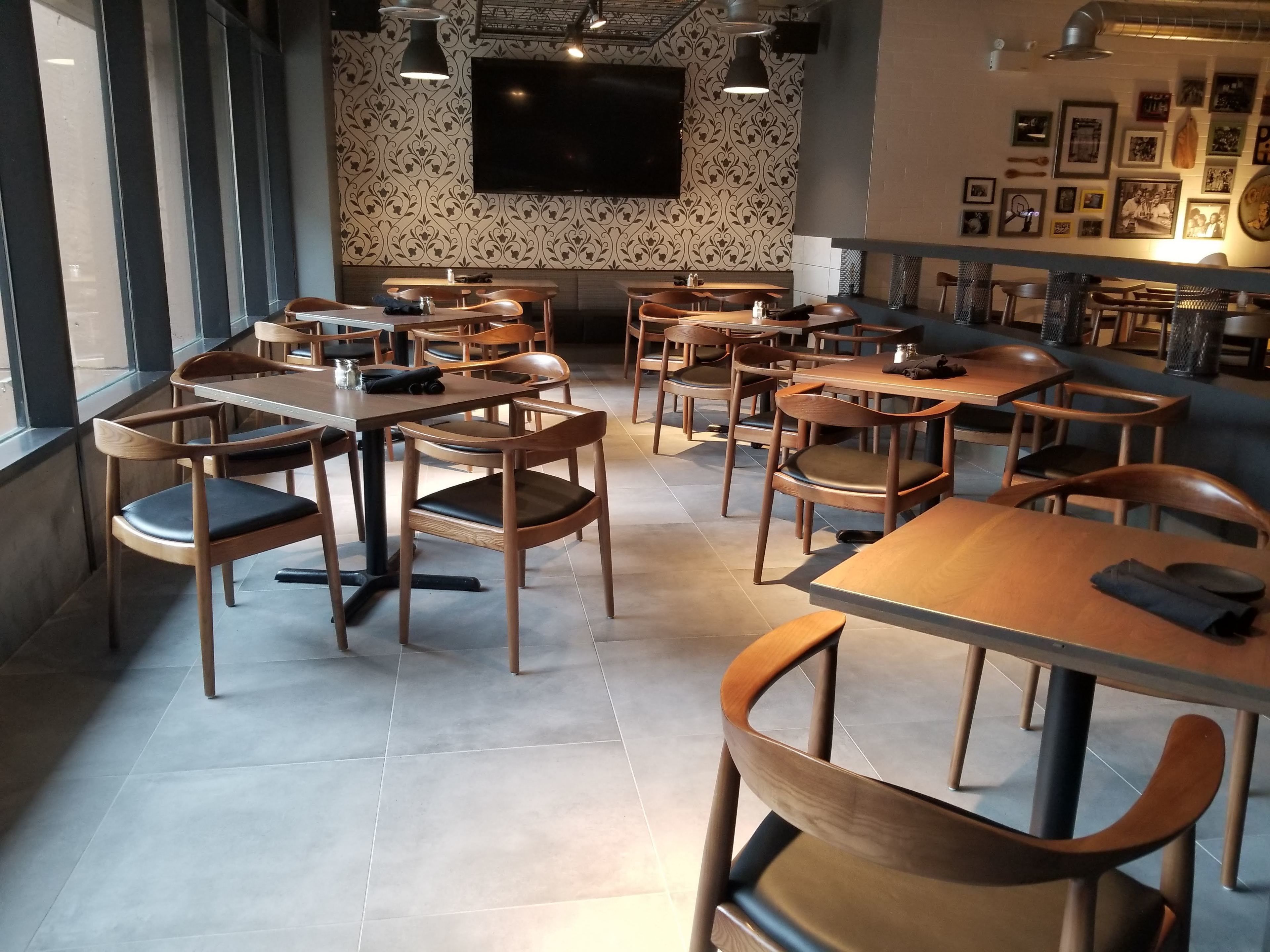 Ein modernes Restaurant-Interieur mit Holztischen und -stühlen, einem großen Fernseher an der Wand und gerahmten Bildern an den Wänden.