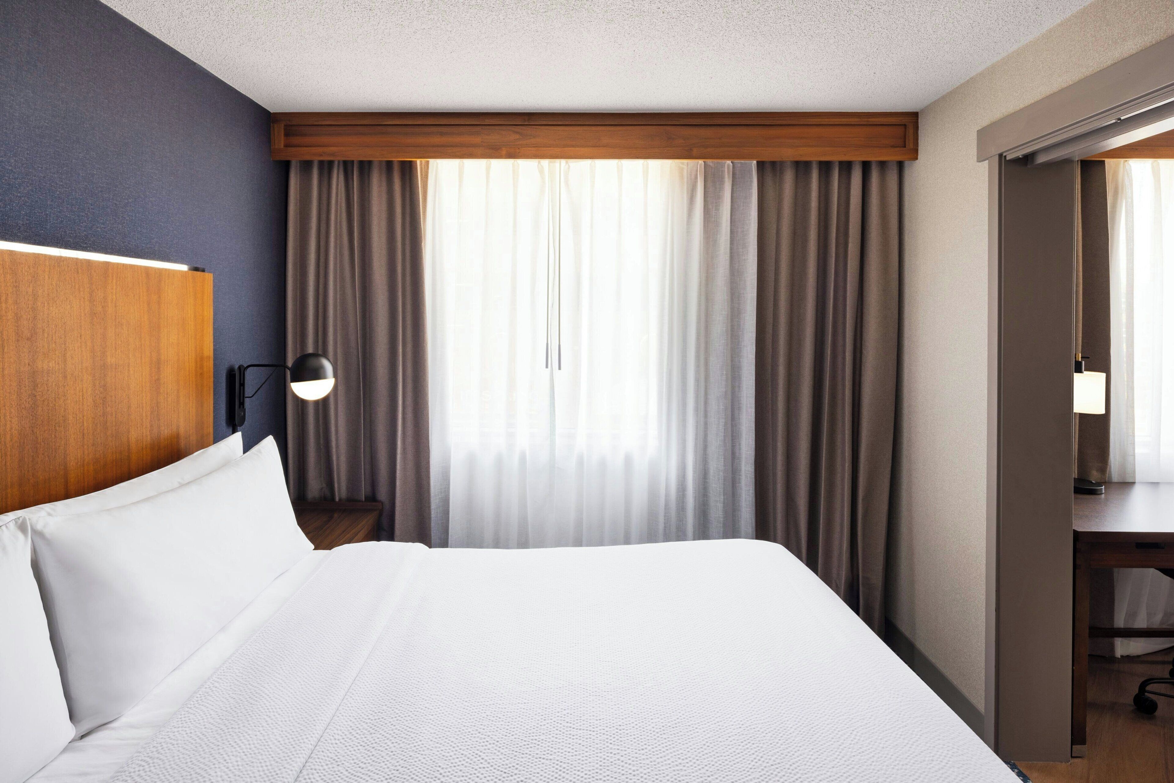 A hotel room with a bed, a desk, a lamp, and curtains.