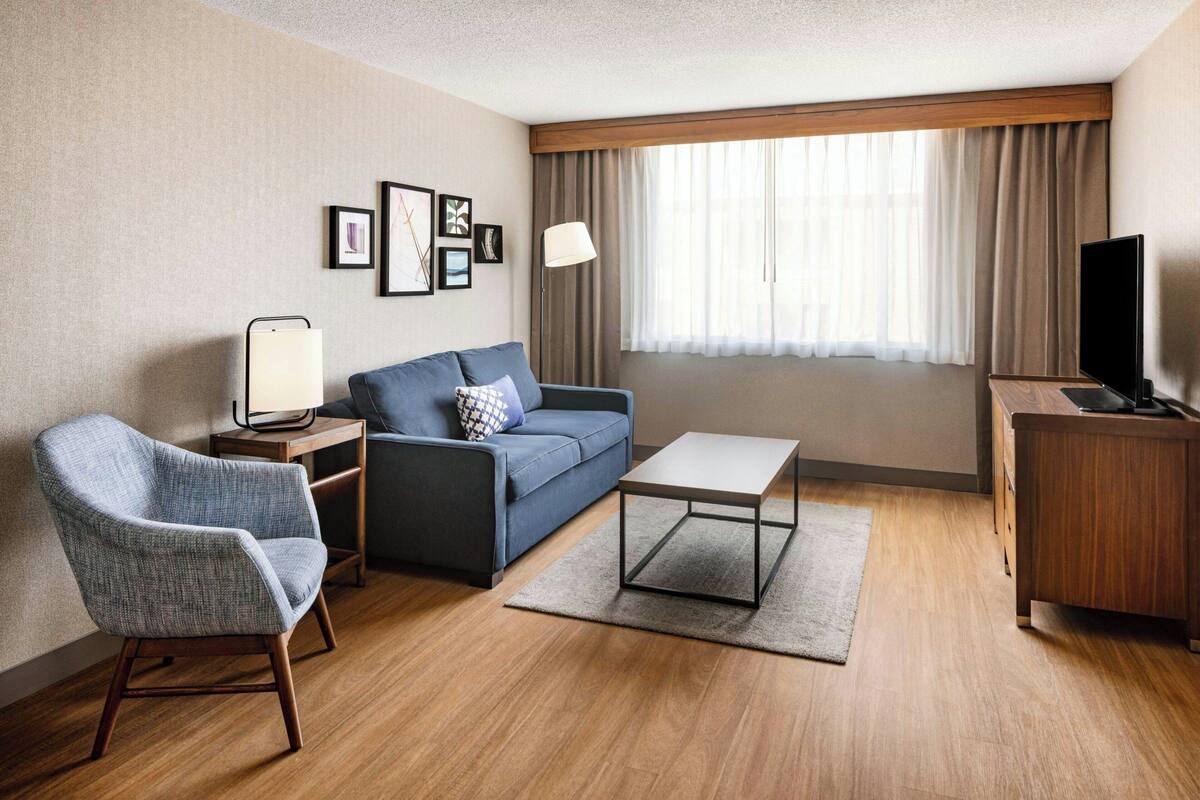 A hotel room with a sofa, armchair, coffee table, TV, lamp, and framed pictures on the wall.