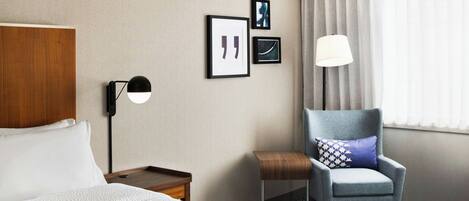 Une chambre d’hôtel avec un lit, une chaise, une table de chevet, une lampe et des tableaux encadrés au mur.