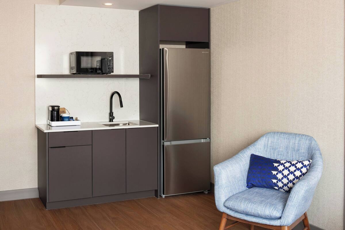 A compact kitchen with a stainless steel refrigerator, a microwave, and a sink.