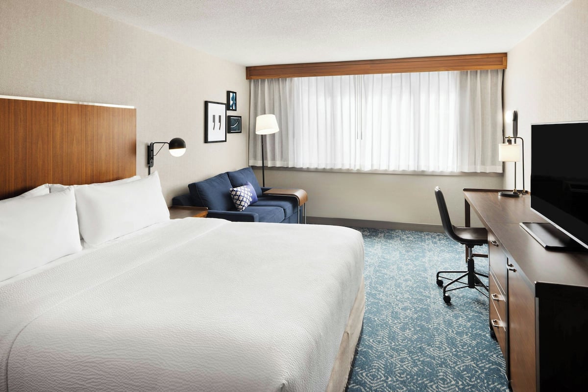 A hotel room with a large bed, a desk, a chair, a television, and a window with curtains.