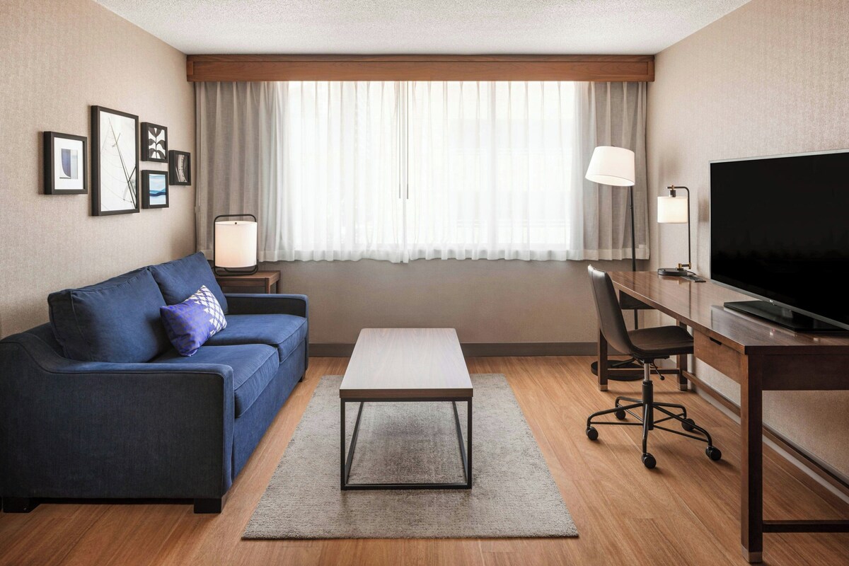 A hotel room with a sofa, a small table, a TV, a desk, and a chair.