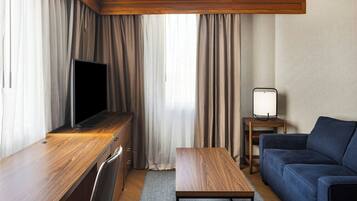 A hotel room with a wooden desk, a television, a sofa, and a small table.