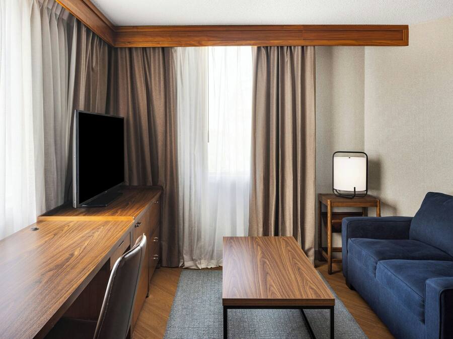 A hotel room with a wooden desk, a television, a sofa, and a small table.