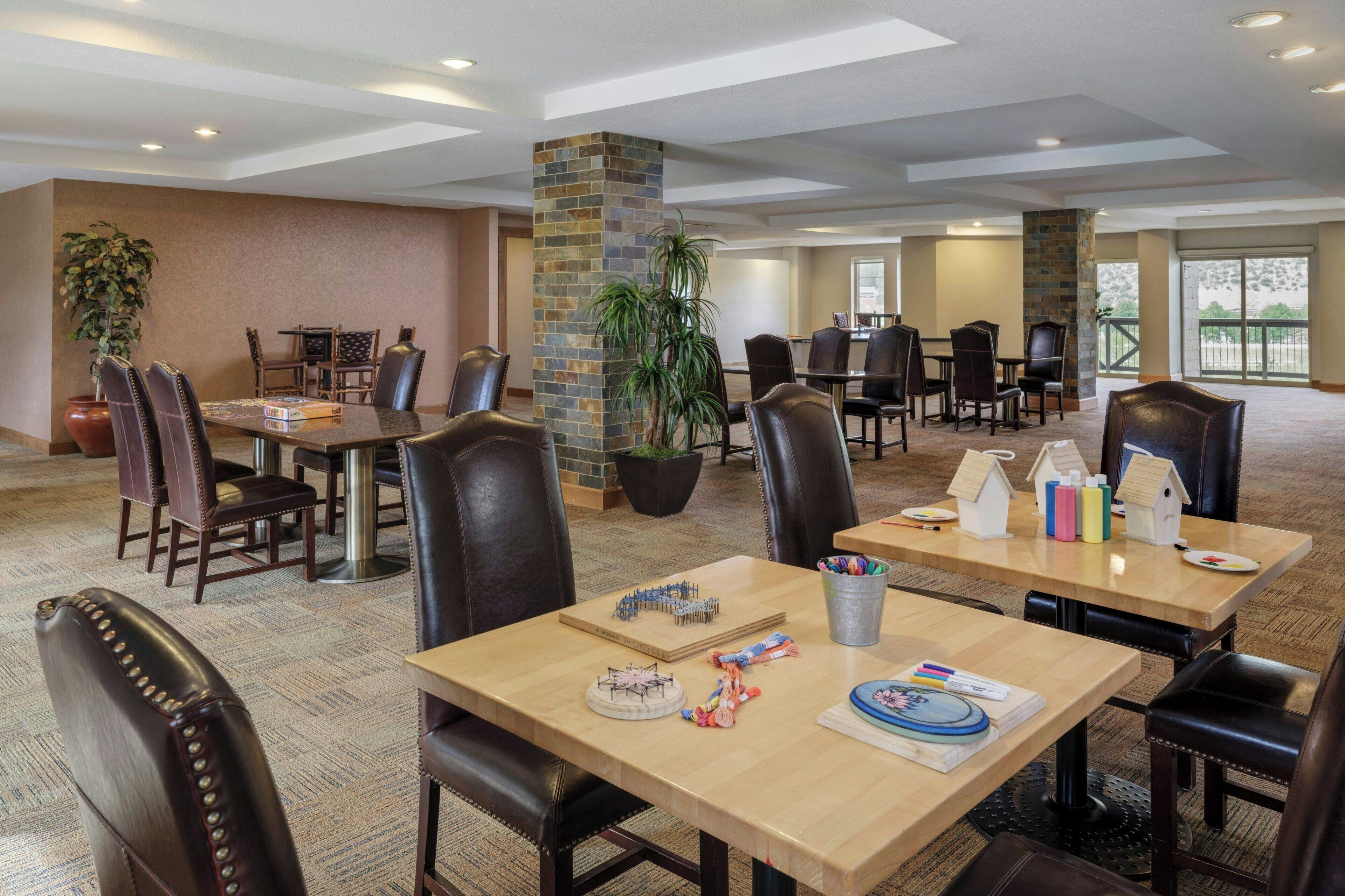 Un vaste espace de restauration dans l’hôtel, avec de nombreuses tables et chaises, un pilier central et des plantes en pot.