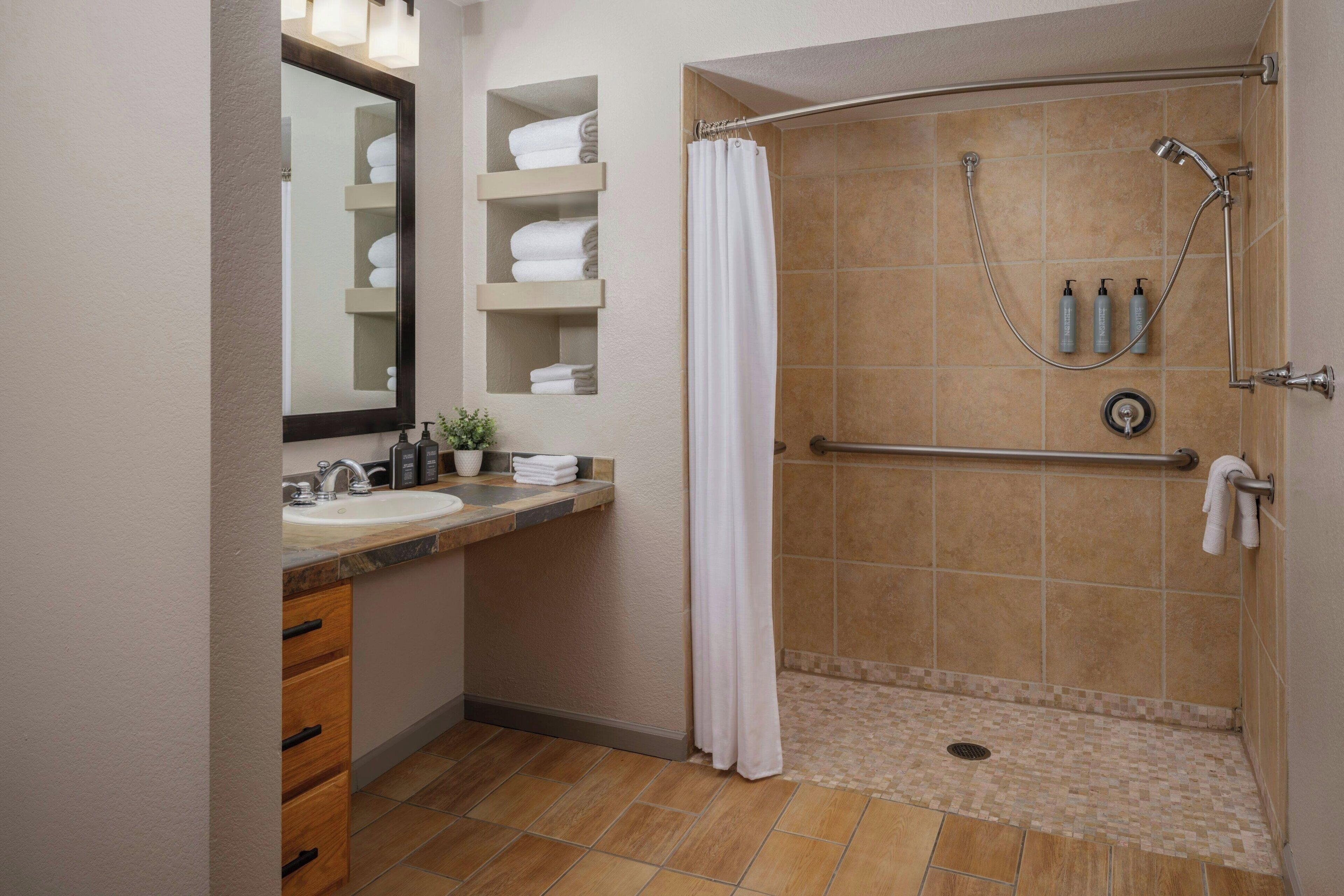 A bathroom with a shower, sink, and storage shelves.
