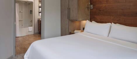 A hotel room with a large bed, wooden wardrobe, and a bathroom visible through an open door.