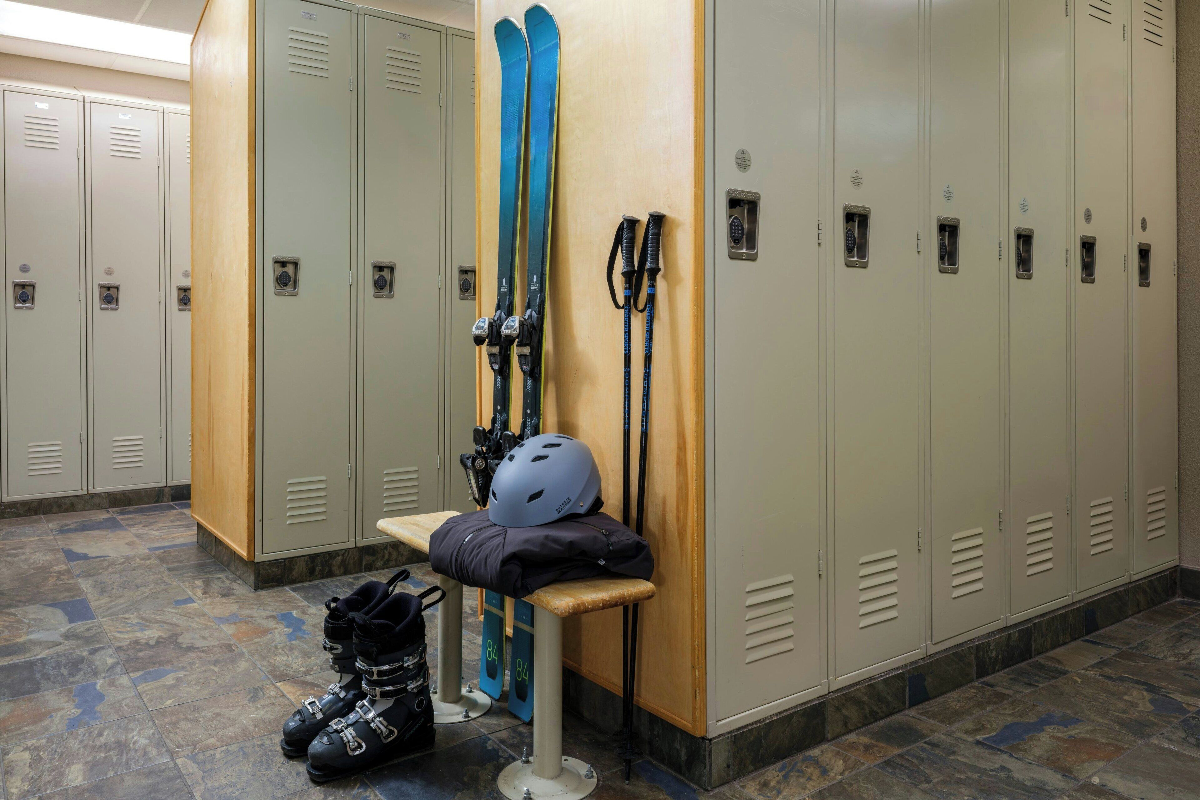 A locker room with multiple lockers, a bench, and skis leaning against the lockers.