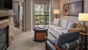 Une chambre d’hôtel avec une cheminée, un canapé, un fauteuil, une télévision et un tableau.