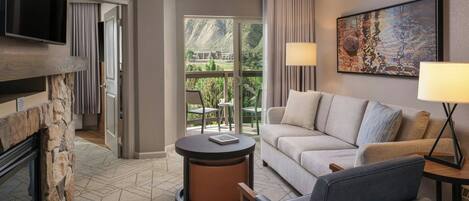 Habitación de hotel con chimenea, sofá, sillón, televisión y un cuadro.