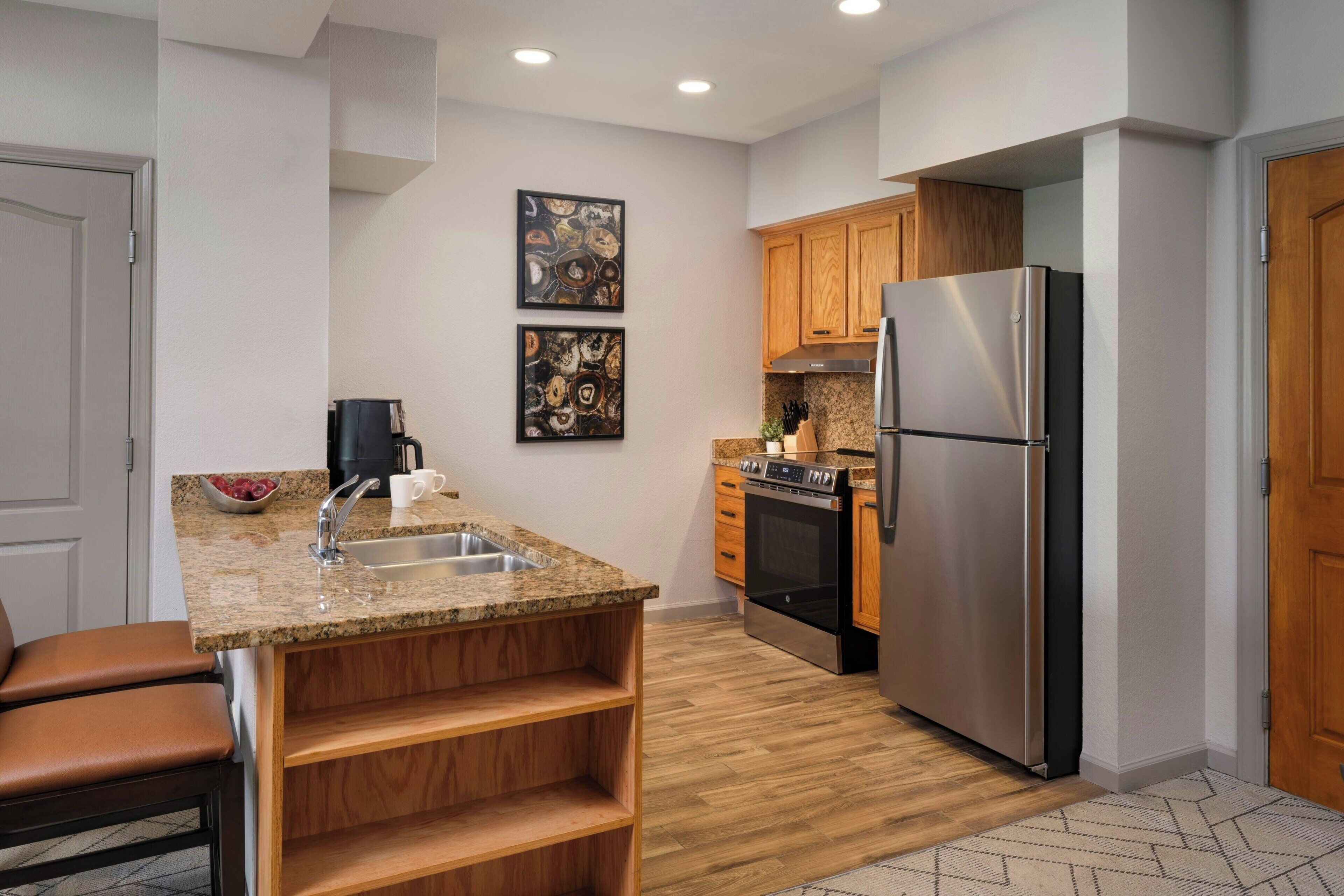 A modern kitchen with granite countertops, stainless steel appliances, wooden cabinets, and a built-in oven.