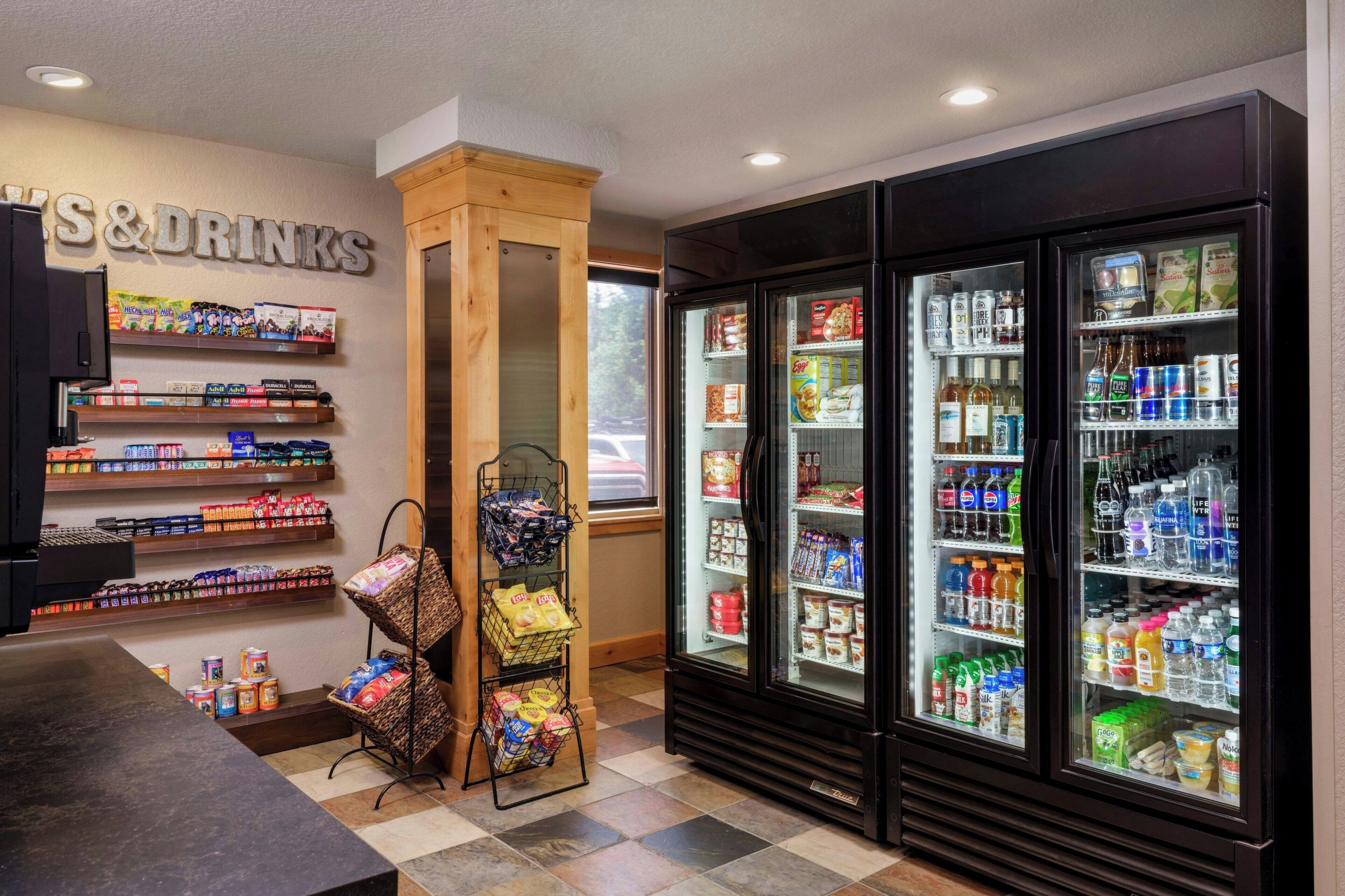 Ein Kiosk mit Regalen voller Snacks, Getränke und sonstiger Artikel. Zwei Kühlregale sind mit Getränken gefüllt und eine Vitrine zeigt Snacks.