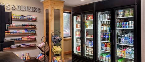 A convenience store with shelves stocked with snacks, drinks, and other items. There are two refrigerators filled with beverages and a display case with snacks.