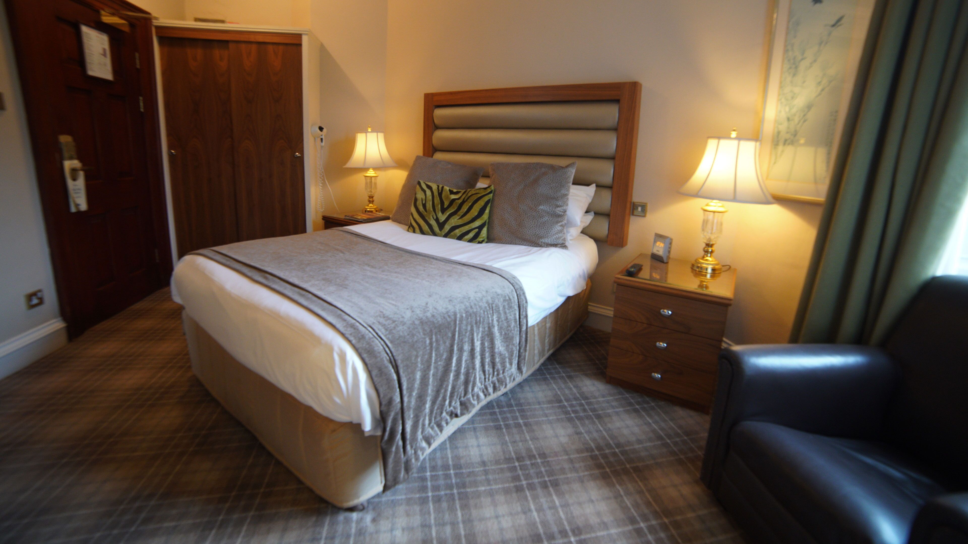 Una habitación de hotel con una cama, dos mesitas de noche, una silla y una puerta.