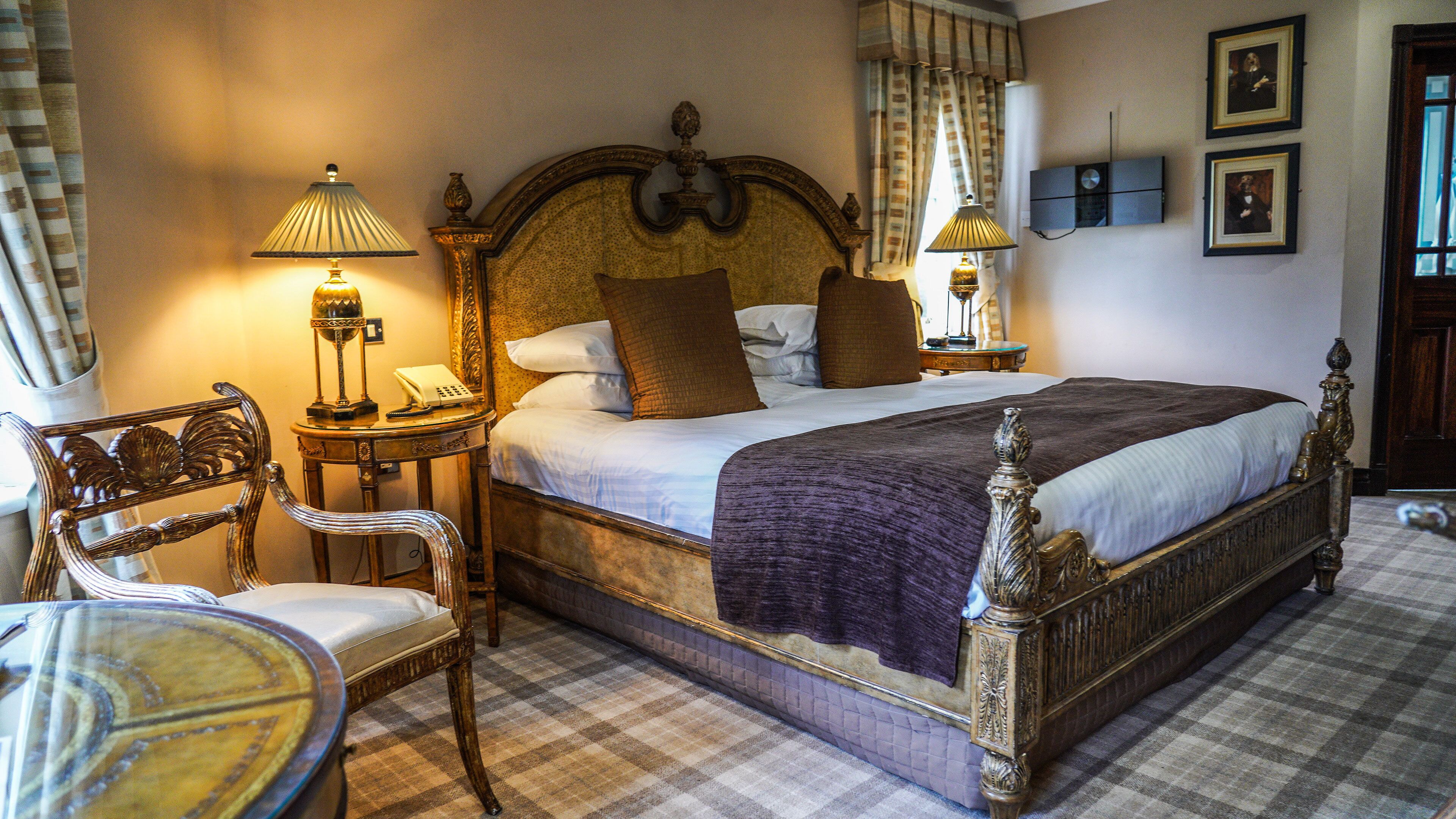 A neatly made bed with a headboard, two bedside tables with lamps, a chair, and a checkered floor.