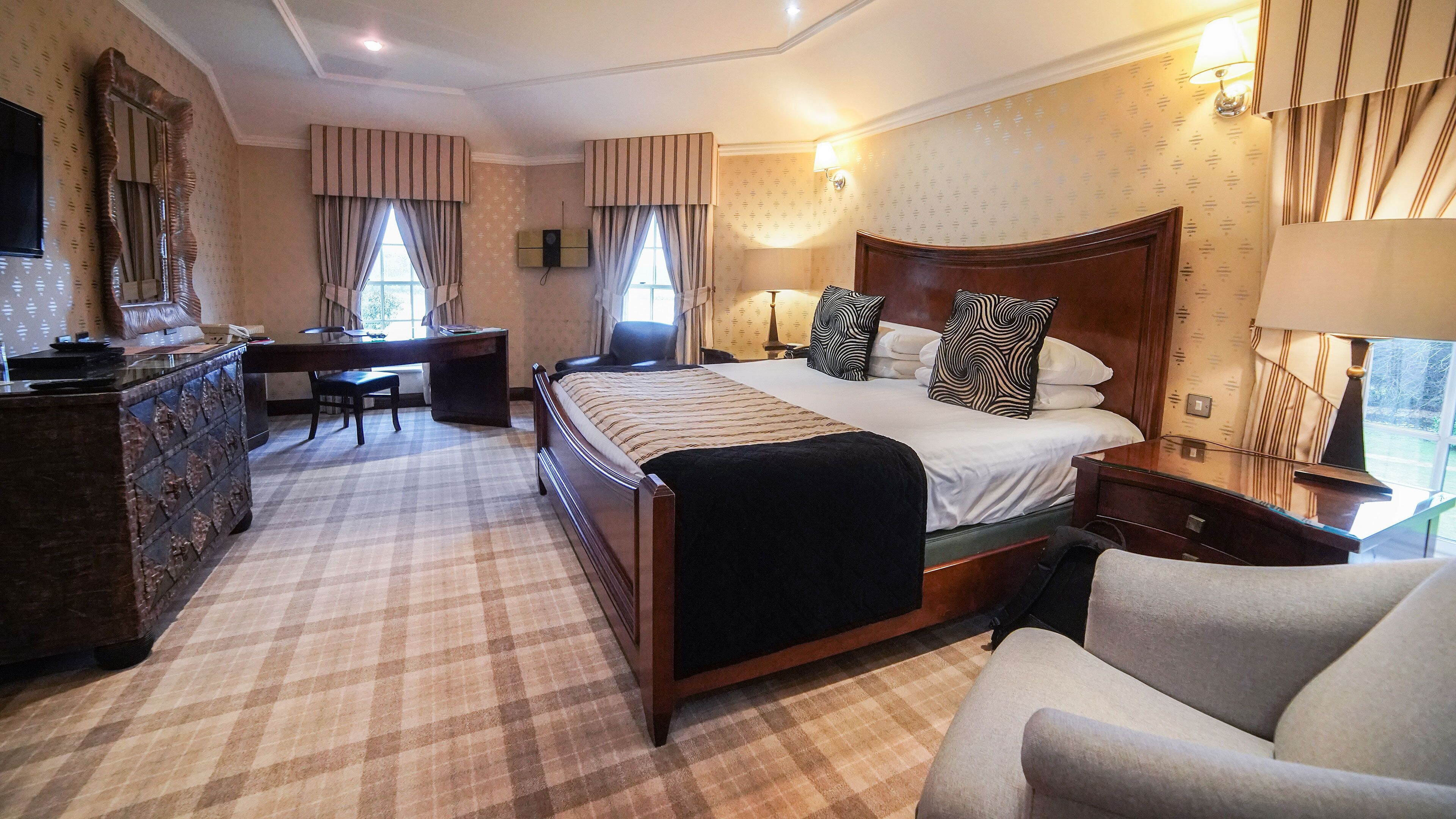 A hotel room with a large bed, a desk, a chair, a dresser, and a TV.
