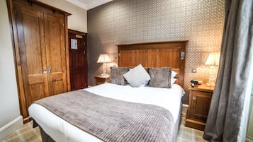 Habitación de hotel con una cama grande, armario de madera, dos mesitas de noche con lámparas y papel tapiz estampado.