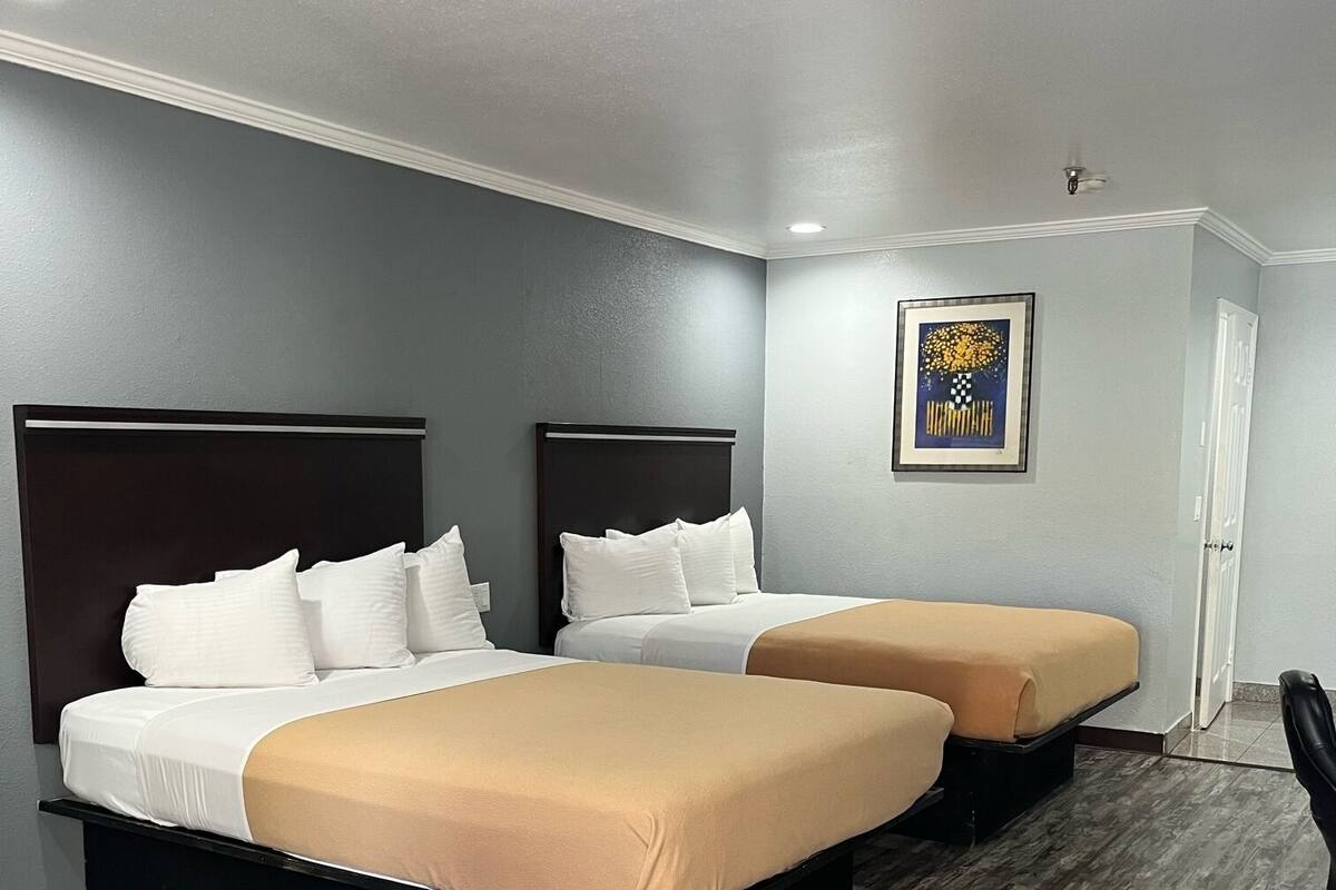 A hotel room with two beds, a wooden floor, and a painting on the wall.