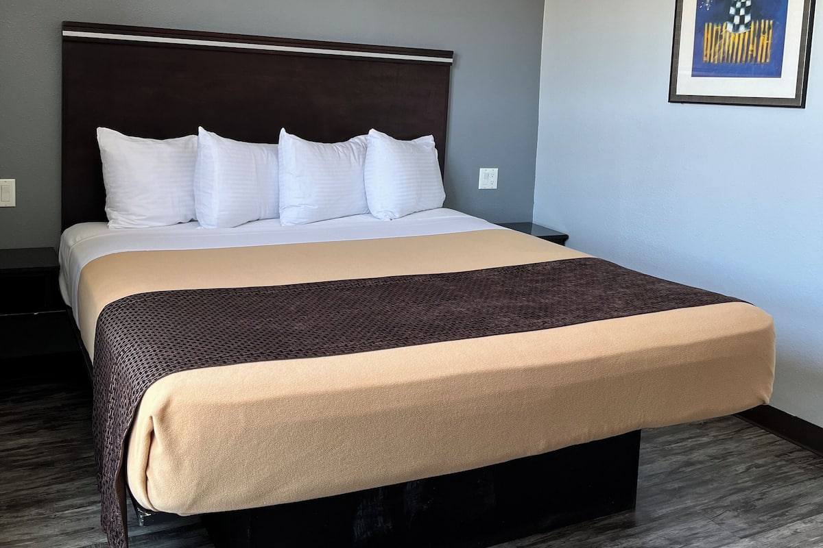 A hotel room with a large bed, dark headboard, and a framed picture on the wall.