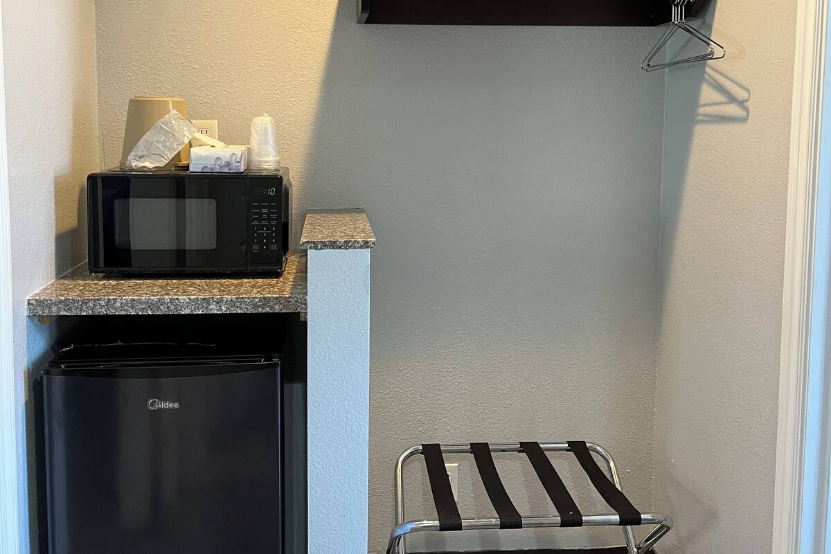 A compact kitchenette with a microwave, a small refrigerator, and a metal drying rack.