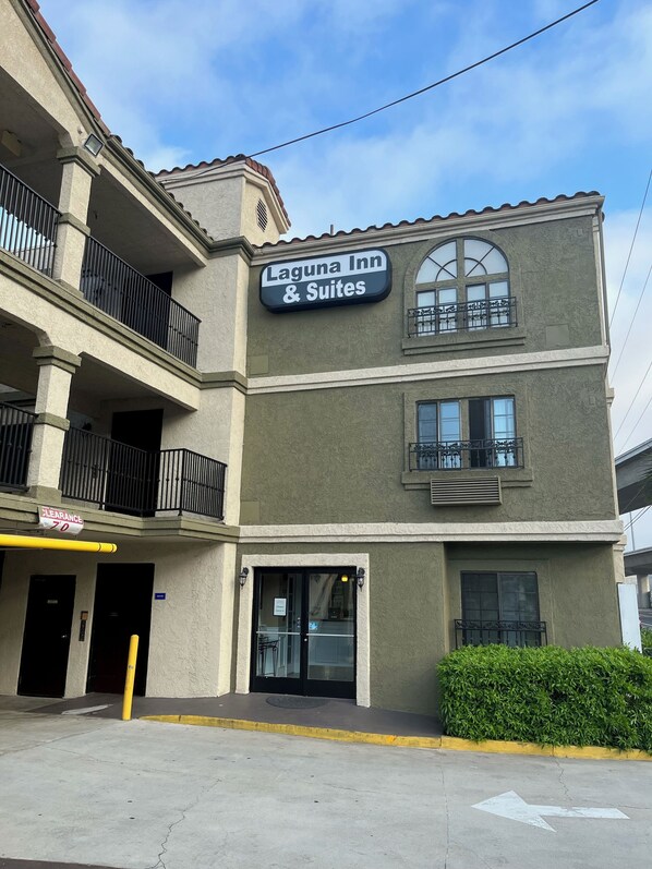 A building with a sign for Laguna Inn & Suites, featuring balconies, a clear sky, and a yellow curb. -  Laguna Inn & Suites (San Juan Capistrano)