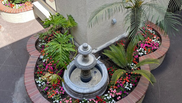 A fountain with a decorative top, surrounded by a circular brick border and colorful flowers. -  Laguna Inn & Suites (San Juan Capistrano)