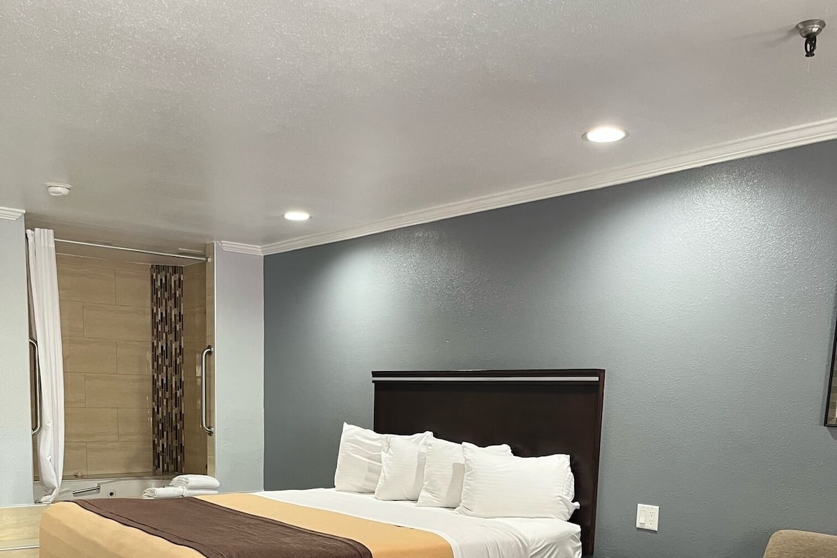 A modern hotel room with a large bed, a separate sitting area, and a shower area.