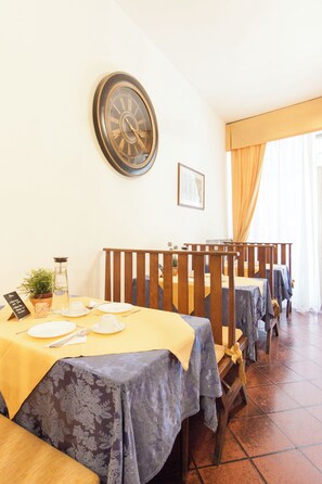 A dining area with tables set for two, a wall clock, and a window with curtains. - Hotel Rex (Florence)