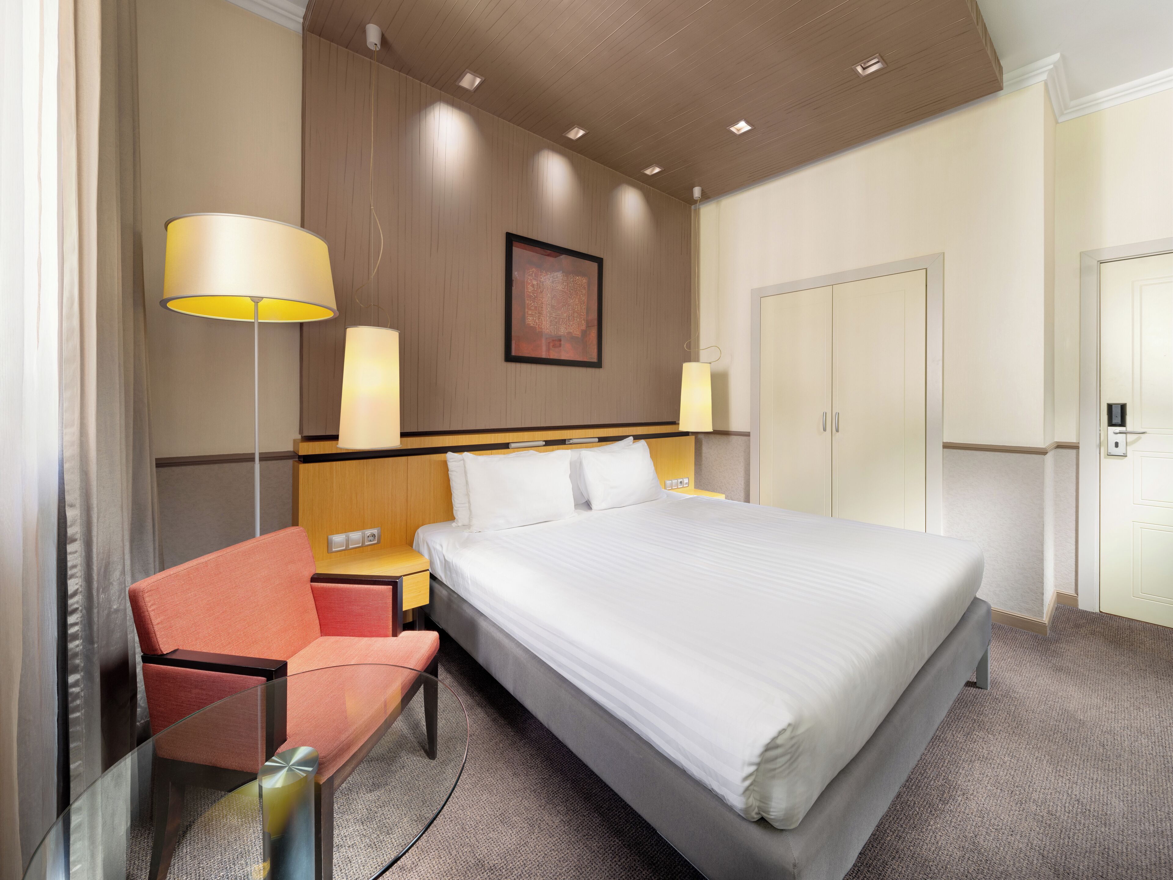 A hotel room with a bed, a desk, a chair, a wardrobe, and two wall-mounted lamps.