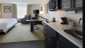 Habitación de hotel con cama, escritorio, silla, televisor, microondas, cafetera y lavamanos.