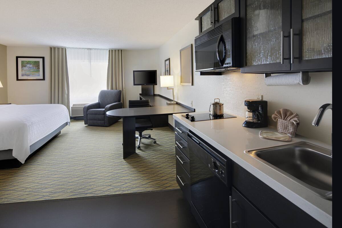 A hotel room with a bed, a desk, a chair, a television, a microwave, a coffee maker, and a sink.