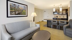 Una habitación de hotel moderna con un sofá gris, una mesa redonda y un comedor con cocina al fondo.