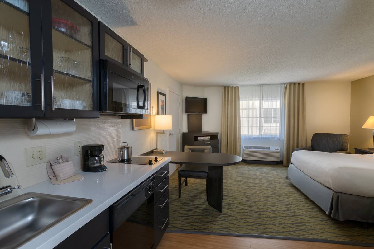 A hotel room with a kitchenette, a bed, a desk, and a TV.