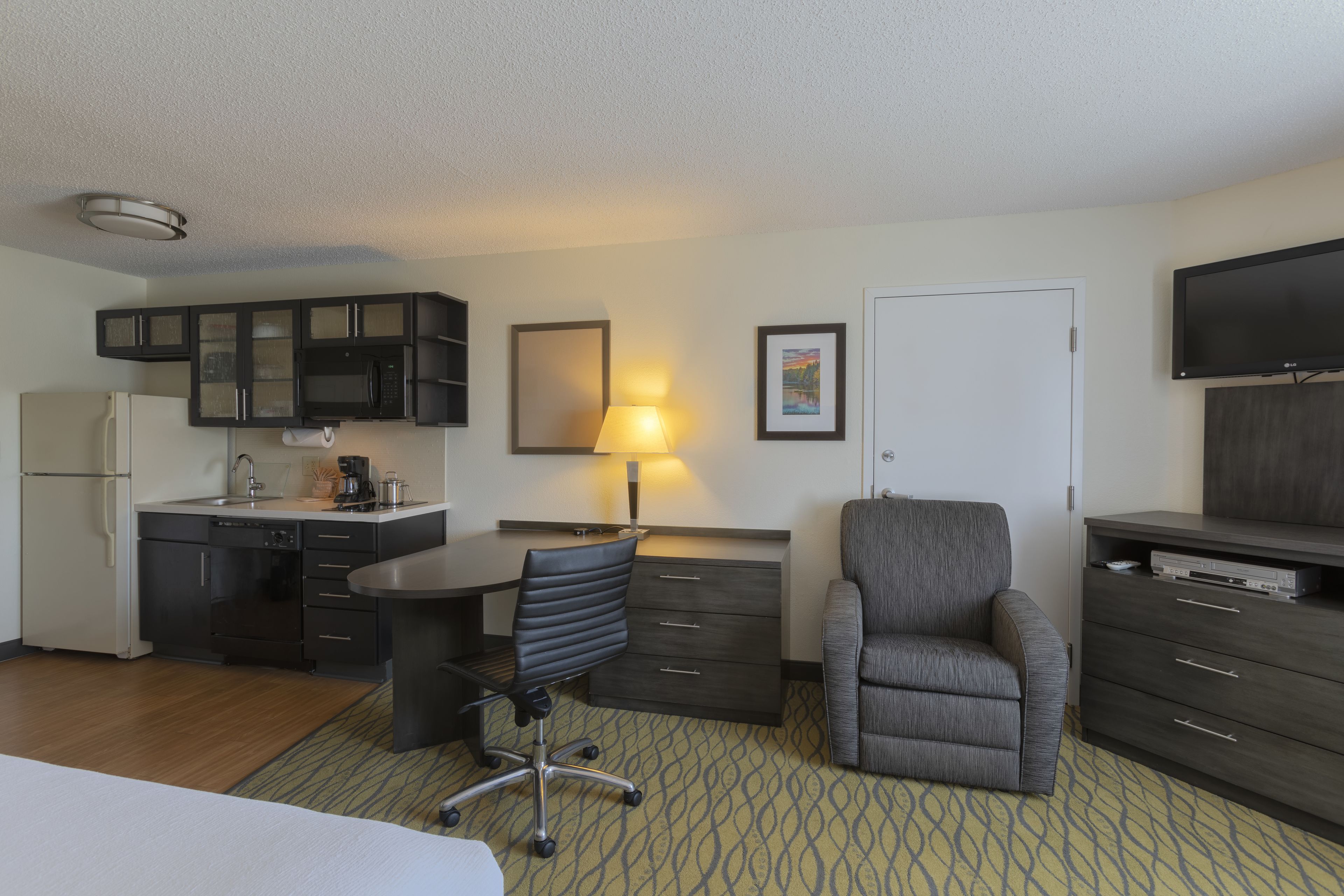A hotel room with a kitchenette, a dining area, a TV, and a bed.