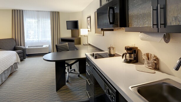 Habitación de hotel con cama, escritorio, kitchenette, televisor y ventana con cortinas.