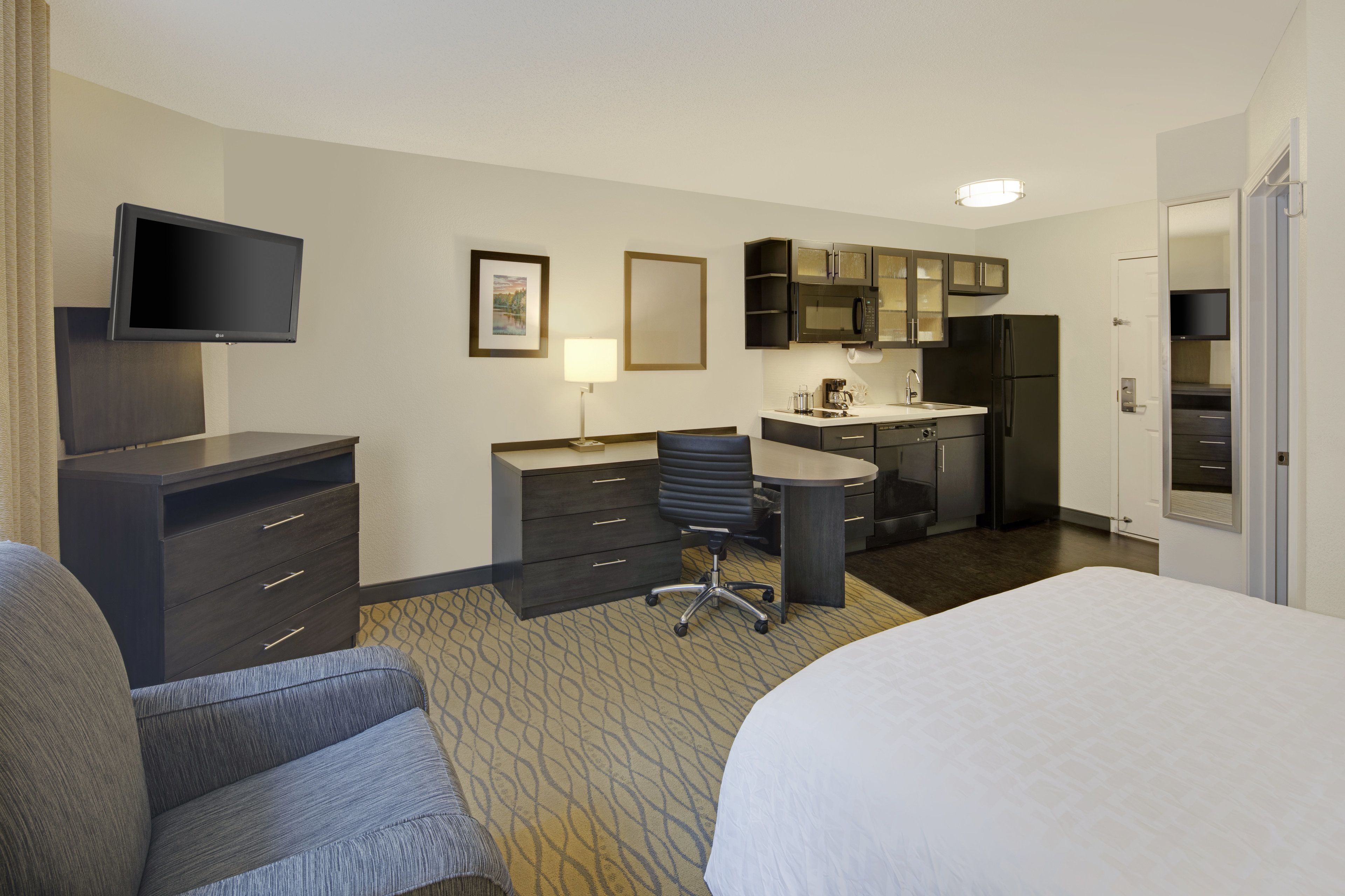 Une chambre d’hôtel équipée d’un lit, d’un bureau, d’une chaise, d’une télévision, d’un four à micro-ondes, d’un réfrigérateur et d’une petite kitchenette.