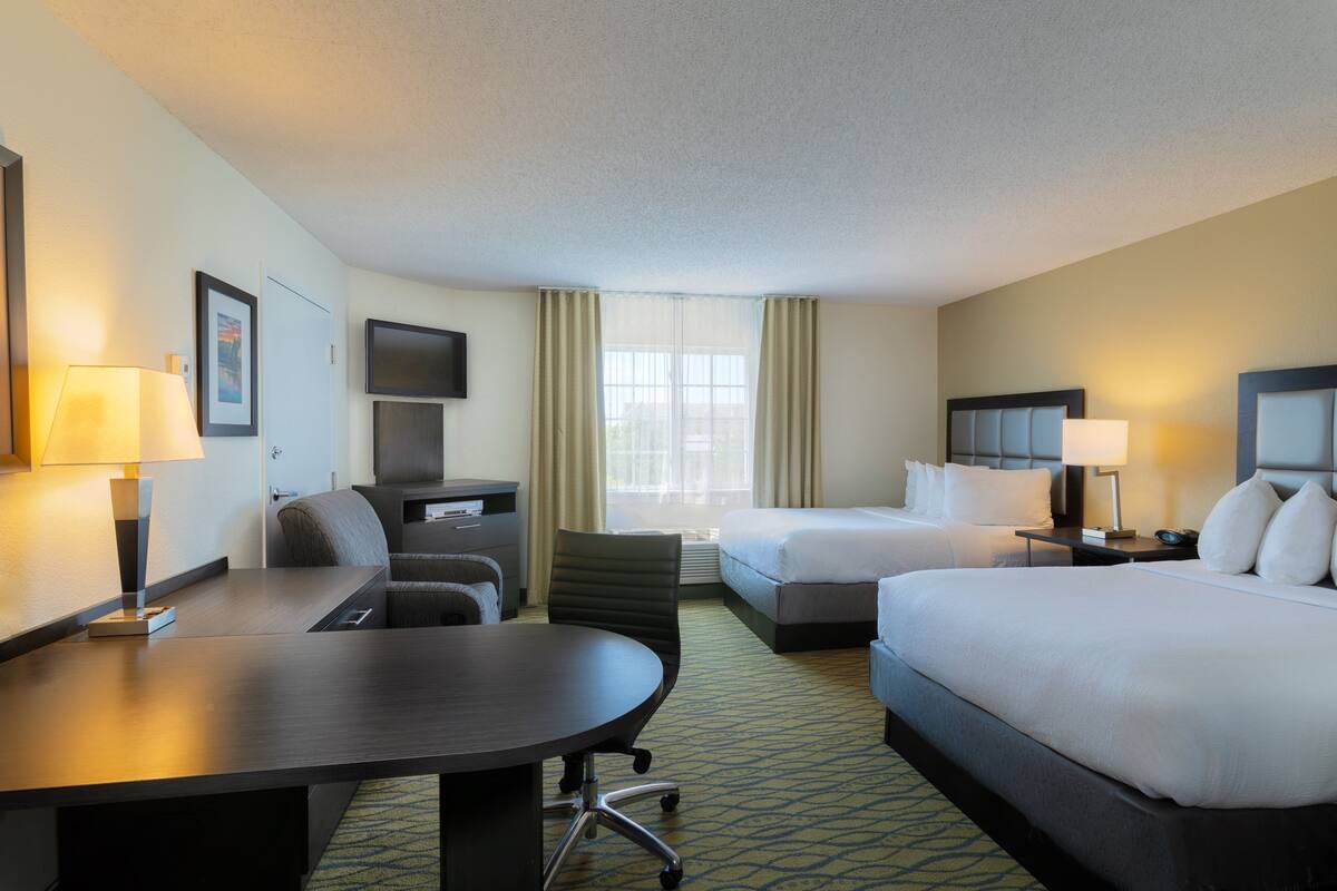 A hotel room with a desk, two beds, a TV, and a window with curtains.